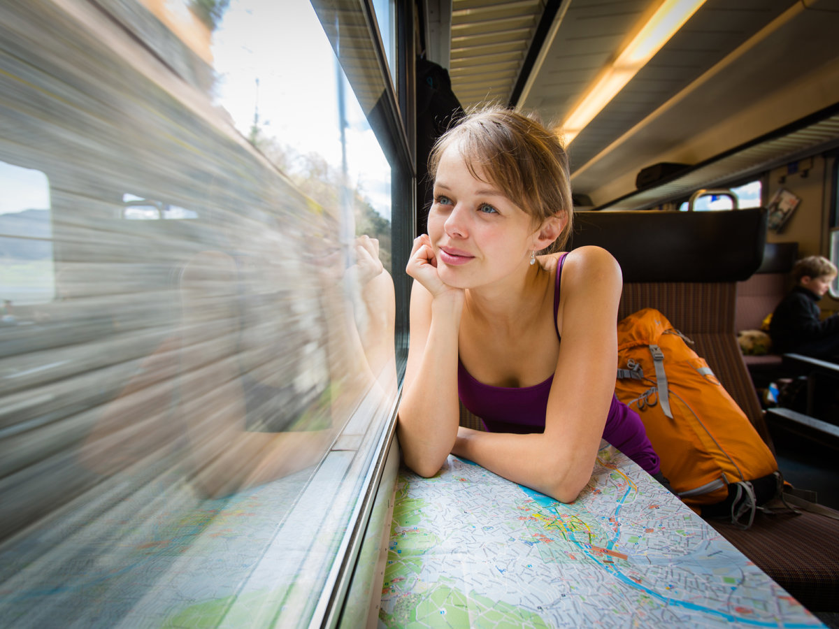 Young female tourist sitting in a Swiss train looking out the window and thinking 