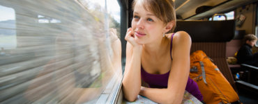 Young female tourist sitting in a Swiss train looking out the window and thinking "Is the Swiss Travel Pass Worth it?" - Swiss Travel Pass reviews, Best travel pass for Switzerland, Switzerland rail pass reviews